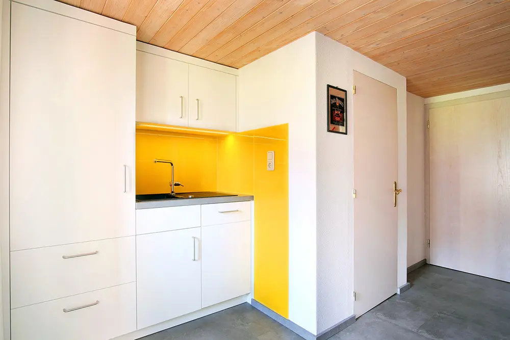 weiße kleine Küchenzeile mit gelben Akzenten an der Wand