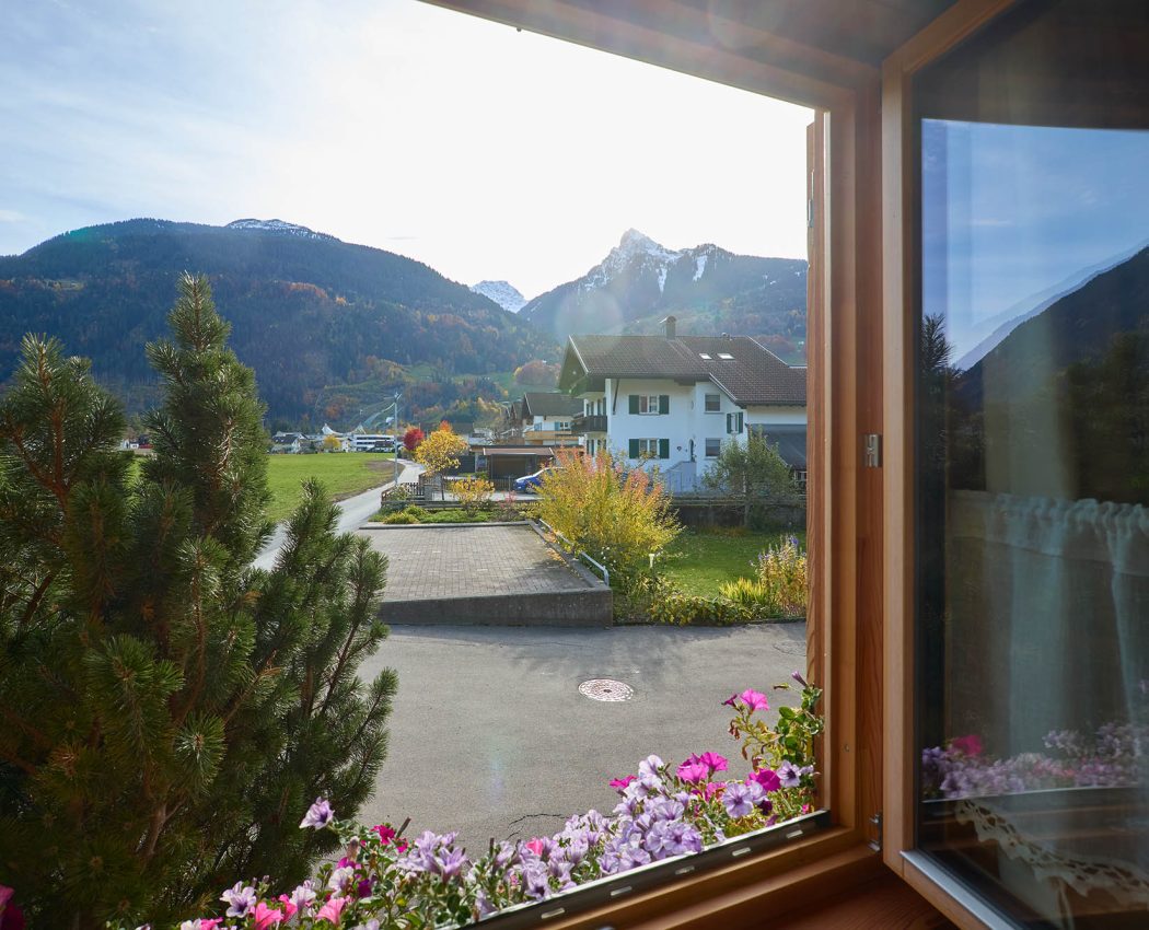 offenes Wohnzimmerfenster mit Blumen und Blick auf den Berg Mittagspitze