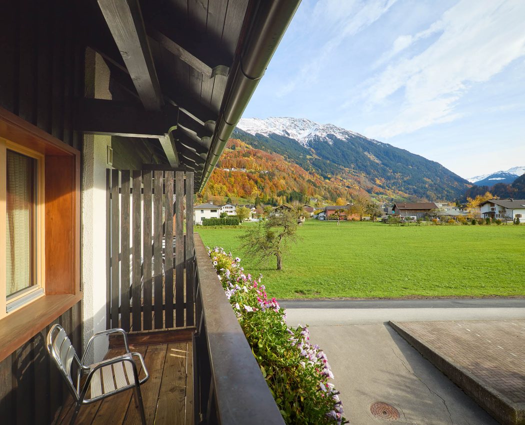 Ausblick vom überdachten Balkon auf eine große Wiese vor dem Bergpanorama Hochjoch