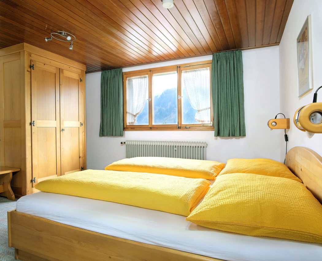 helles Schlafzimmer mit weißen Wänden, Holzdecke, großem Fenster, Kleiderschrank und Doppelbett