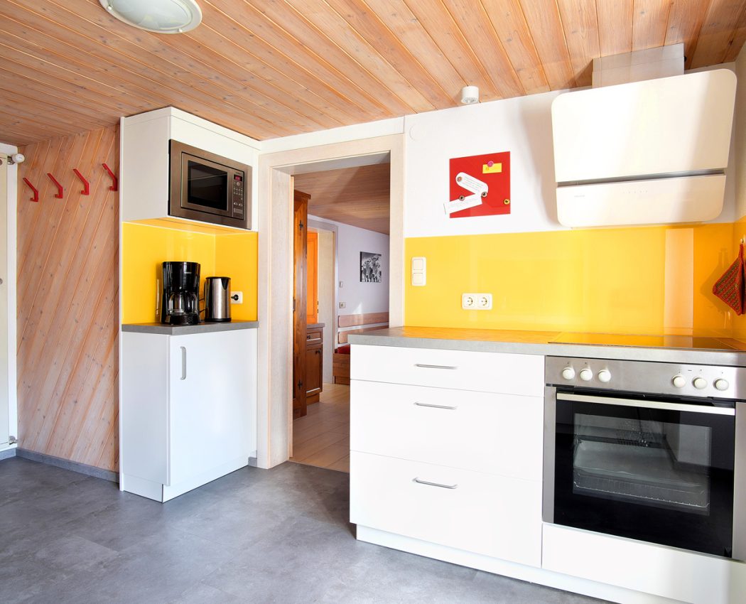 Weiße Küche mit gelben Akzenten und Zugang zum Wohnzimmer
