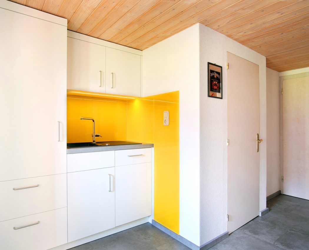 weiße Küchenzeile mit Spüle und gelben Akzenten neben Zimmertür