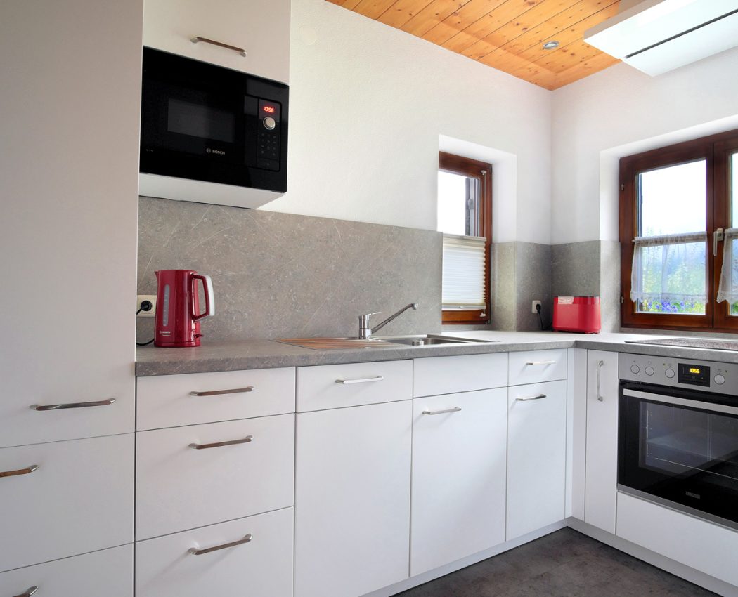 vor zwei Fenstern eine weiße Küchenzeile mit Herd und Spüle