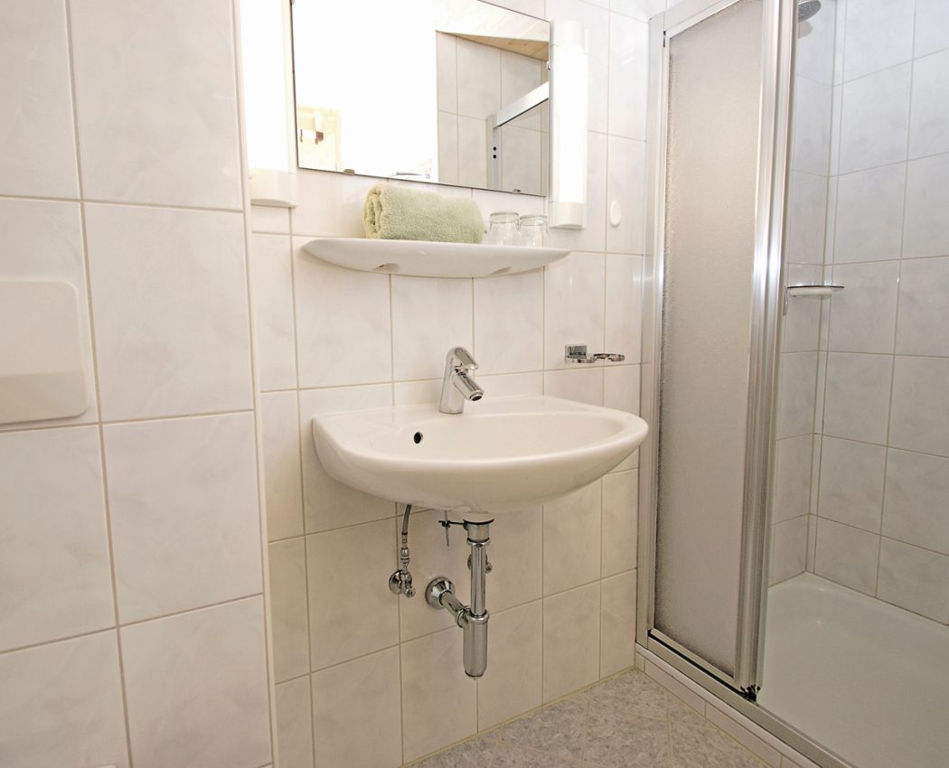 weiß gefließtes Bad mit Wascbecken neben Duschkabine