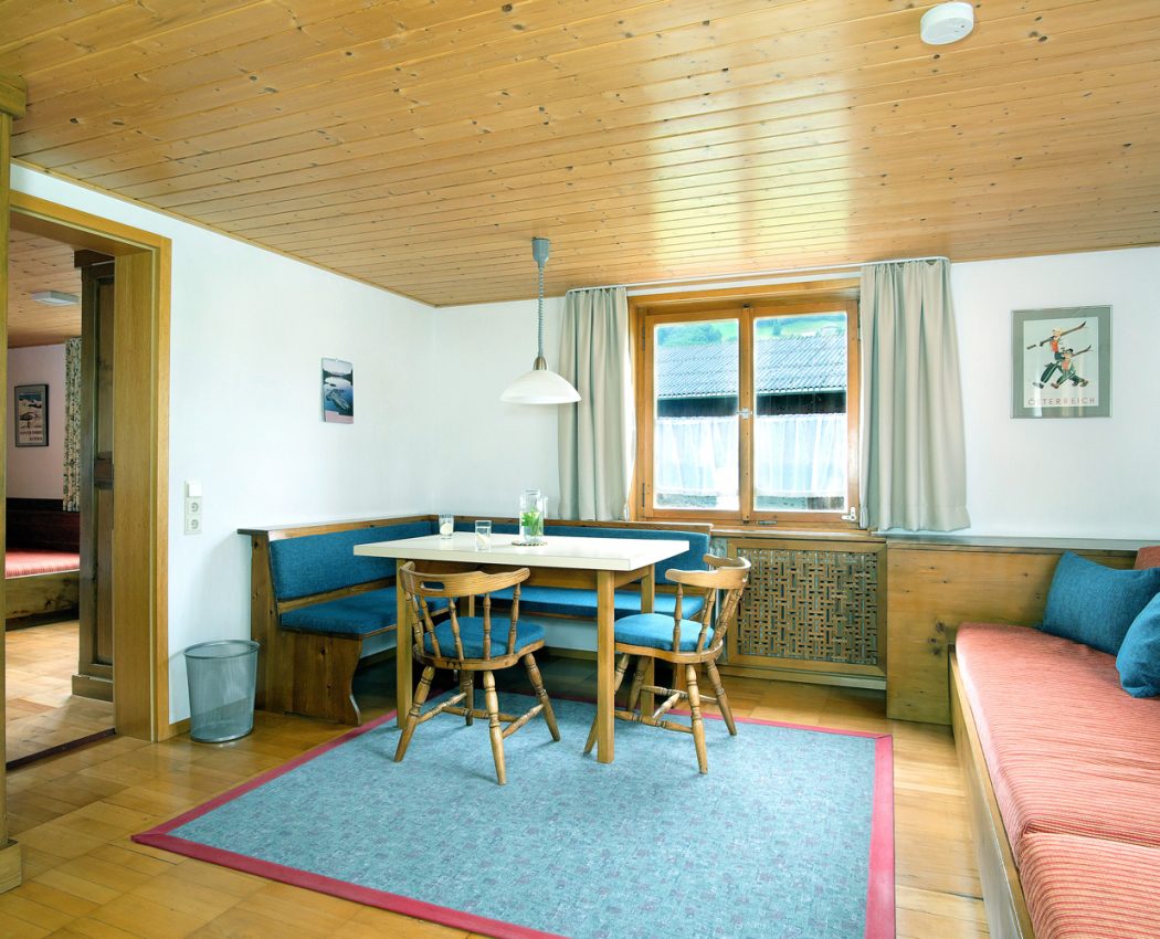 helles Wohnzimmer mit Essecke aus Eckbank und Tisch vor dem Fenster, daneben Bett mit Sofafunktion